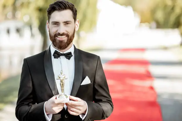 Portrait of an elegant man strictly dressed in tuxedo as a well-known actor standing on the red carpet during the awards ceremony