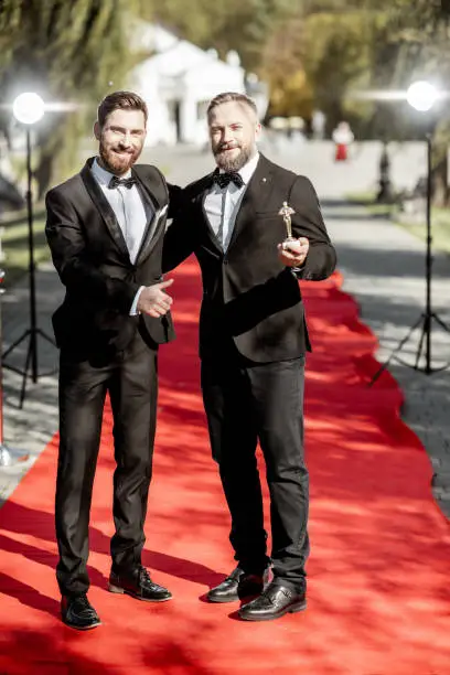 Two elegant men strictly dressed in suits as a well-known film actors having fun during awards ceremony on the red carpet outdoors