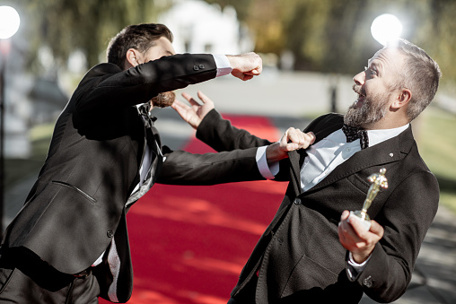 Funny portrait of a two men strictly dressed as a film actors fighting on the red carpet during awards ceremony outdoors