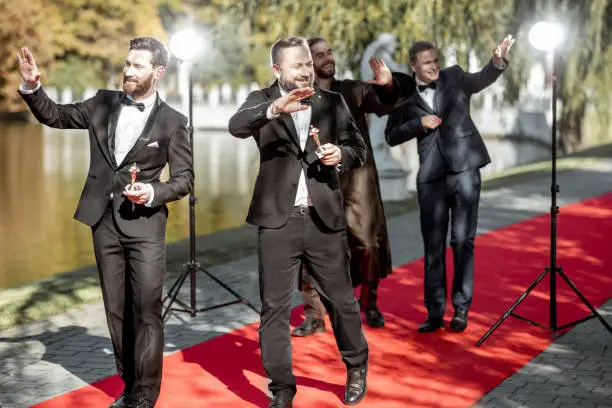 Group of elegant men as a famous movie actors walking on the red carpet and greeting with fan during awards ceremony