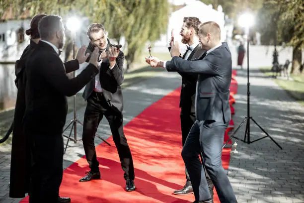 Group of a men as a well-known movie actors and secret agent playing with handgun during awards ceremony on the red carpet outdoors