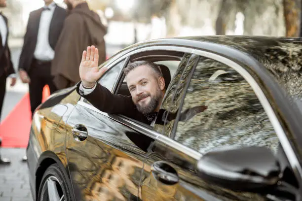 Portrait of a man as a famous movie actor sitting in the luxury car, arriving on the awards ceremony or movie premiere near the red carpet outdoors