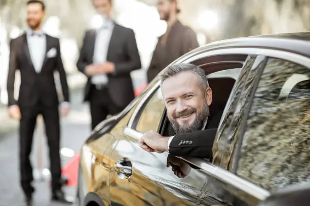 Portrait of a man as a famous movie actor sitting in the luxury car, arriving on the awards ceremony or movie premiere near the red carpet outdoors