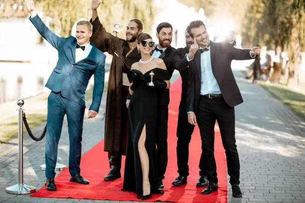 Group portrait of an elegant people as a famous movie actors standing together on the red carpet during awards ceremony outdoors