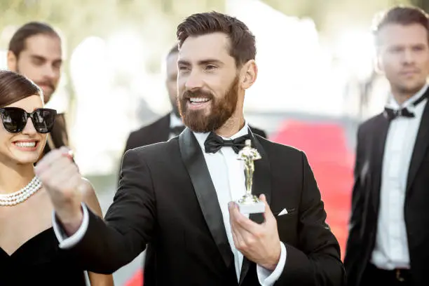 Portrait of an elegant man as a well-known movie actor holding famous Academy Award during awards ceremony on the red carpet outdoors