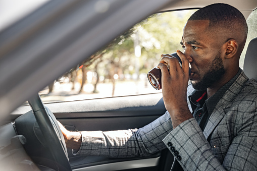 Young African businessman driving car and drink coffee.