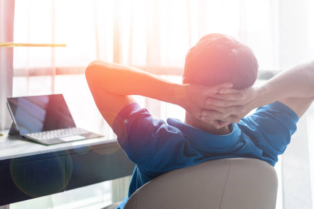 entspannen geschäftsmann lebensstil zu hause sitzen auf modernem stuhl im wohnzimmer blickaus dem fenster schöne stadtbild innenstadt stadtleben mit sonnenlicht-effekt: - hands behind head stock-fotos und bilder