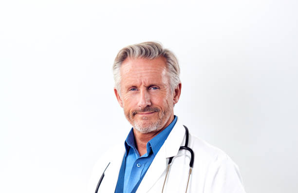 scatto in studio di medico maschio maturo che indossa il camice bianco e lo stetoscopio su sfondo bianco - doctor male doctor mature men portrait foto e immagini stock