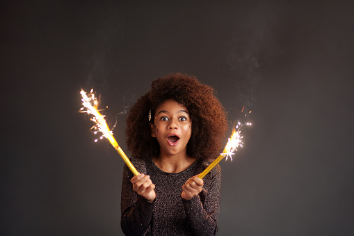 Cute festive girl with burning sparklers against dark background