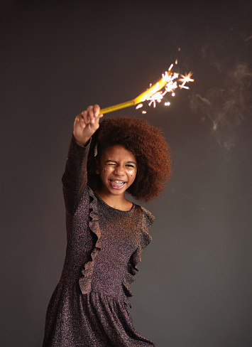 Cute festive girl with burning sparkler against dark background