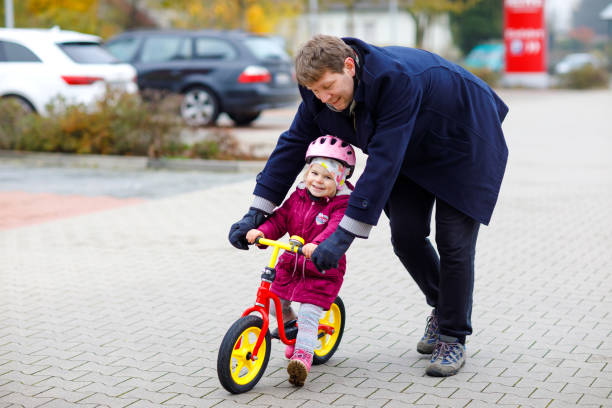 Cute little toddler girl in safety helmet riding on run balance bike. Middle-aged father teaching happy healthy lovely baby child daughter having fun with learning bicycle. Active family outdoors linda niña pequeña en el casco de seguridad que monta en la bicicleta de equilibrio de carrera. padre de mediana edad enseñando feliz saludable encantadora hija bebé divirtiéndose con el aprendizaje de la bicicleta. familia activa al aire libre.