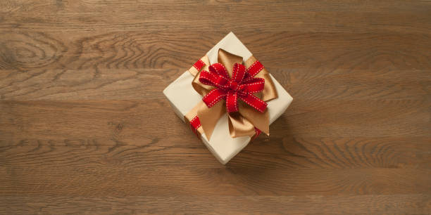 Boîte de cadeau de Noel attachée avec l'arc rouge et d'or au-dessus d'une table en bois. Composition horizontale avec espace de copie à gauche et à droite de la boîte. - Photo