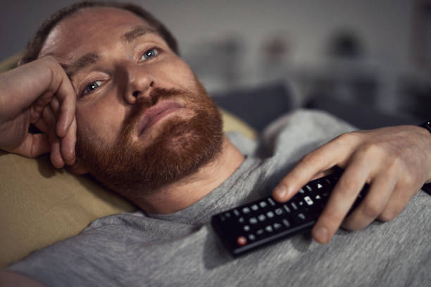 sleepy man ver tv en couch - television boredom men sofa fotografías e imágenes de stock