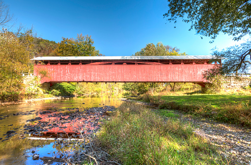 Old covered bridge processed using HDR in rural Bedford County, Pennsylvania, USA taken in early Autumn as the leaves are just starting to change with a rich blue sky in the background.