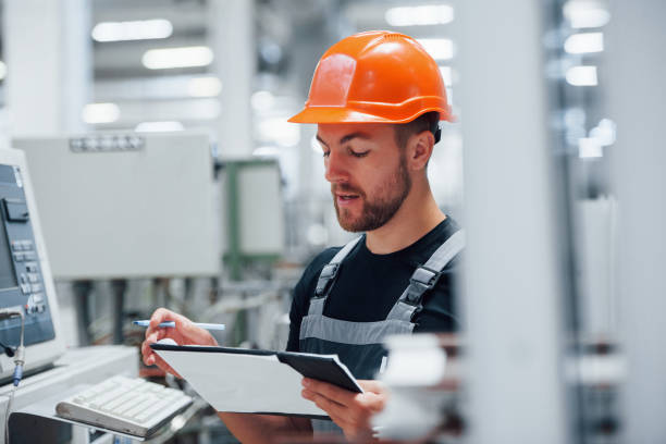 istock Making notes. Industrial worker indoors in factory. Young technician with orange hard hat 1186930638