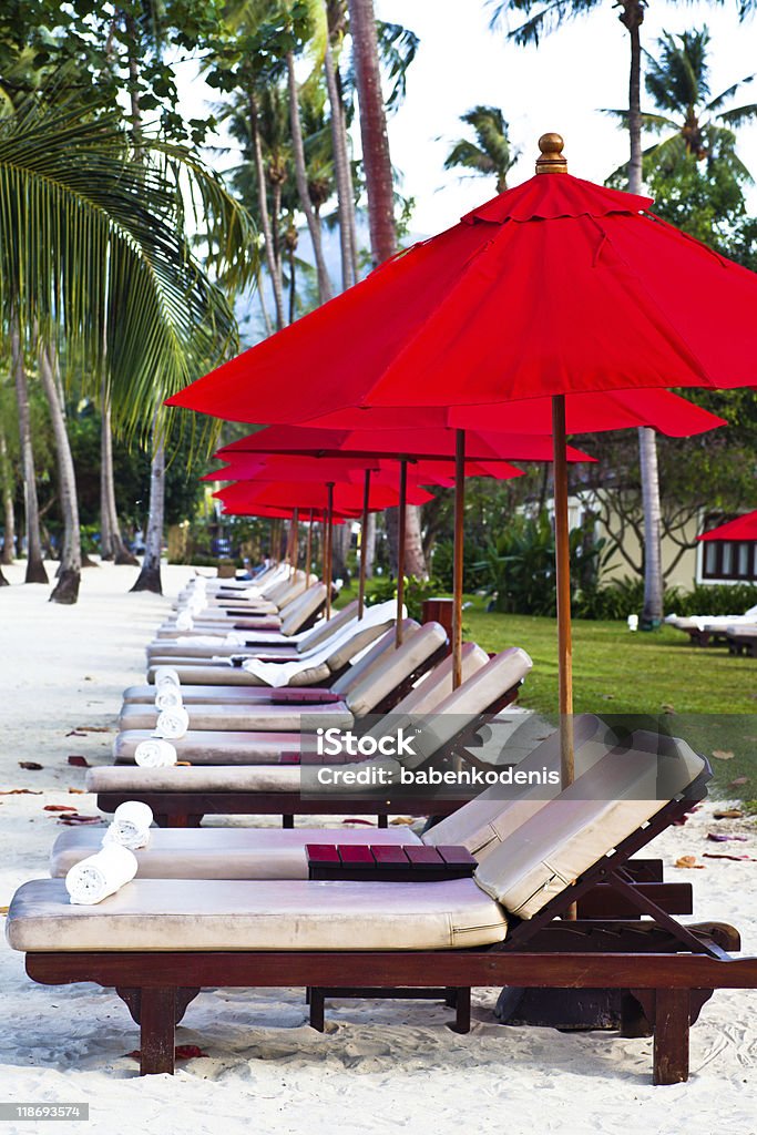 Rojo, sombrillas y sillas reclinables en la playa de arena en el Trópico - Foto de stock de Playa libre de derechos