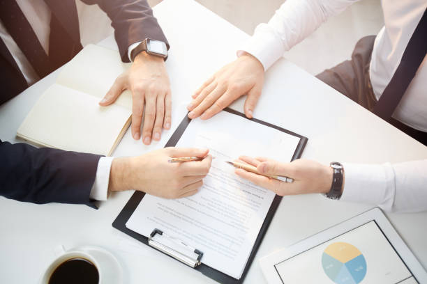 istock Unrecognizable businessmen in formalwear sitting at table and pointing at papers while discussing partnership contract at meeting 1186935859