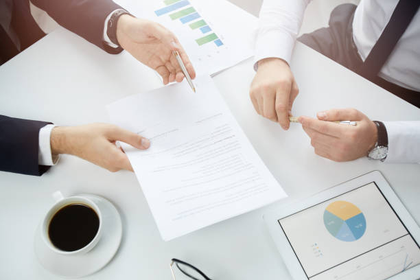 istock Above view of unrecognizable businessman sitting at table and pointing at contract while leading negotiation with investor 1186935918