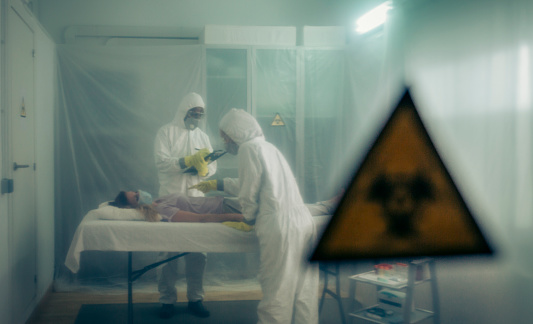 Two people attending to a woman with a virus lying on a stretcher in a field hospital with bio hazard symbol in the foreground