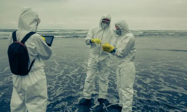 People with bacteriological protection suits analyzing seawater on the beach