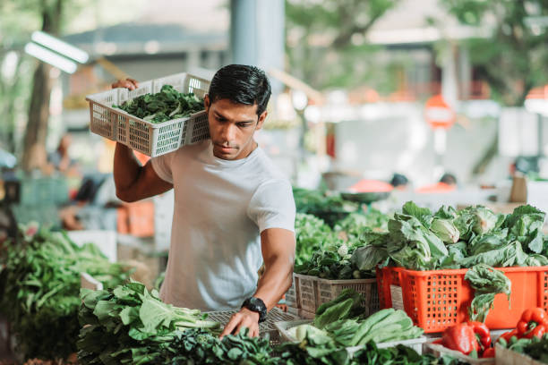 Asian malay male carrying big basket of vegetable on his shoulder and selecting freshness of vegetable at his own stall stock photo