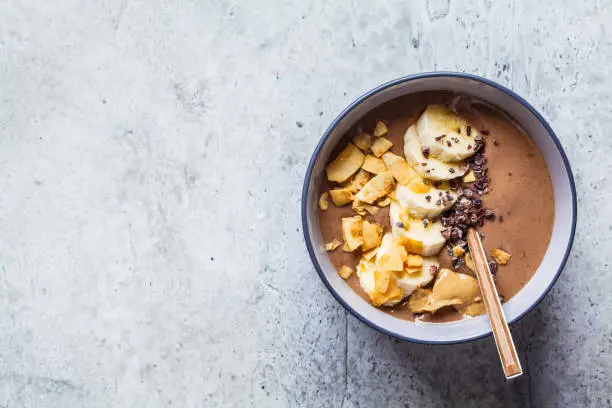 Photo of Chocolate smoothie bowl with banana, coconut and chocolate in a gray bowl, top view.