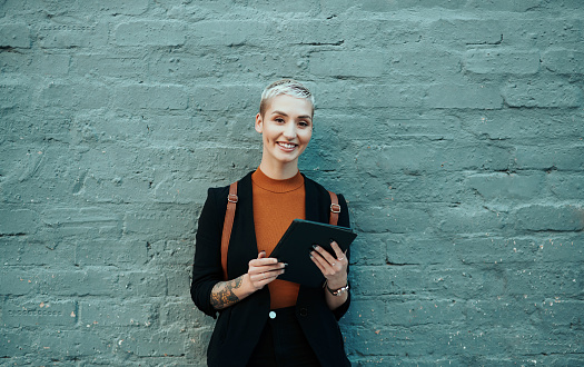 Portrait of an attractive young creative businesswoman using a digital tablet while standing against a grey wall outdoors