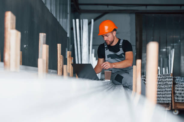 istock Using silver colored laptop. Industrial worker indoors in factory. Young technician with orange hard hat 1186939624