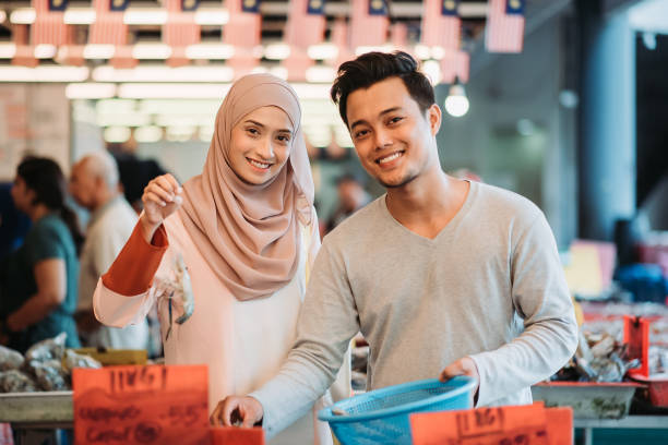 Asian malay couple carrying a basket of prawn, picking up a prawn and looking at camera with smiling face during morning wet market shopping togetherness on morning market shopping happy malay couple stock pictures, royalty-free photos & images