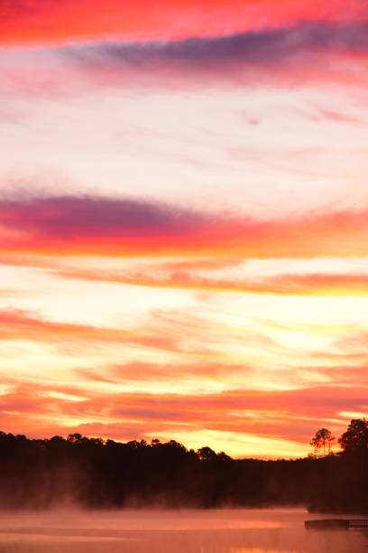 istock Bright orange sunlight on pre-dawn clouds over forest with lake pier at frame edge 1186943719