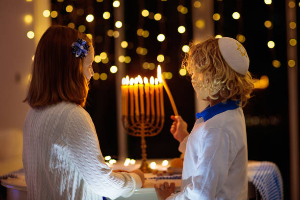 Kids celebrating Hanukkah. Festival of lights. Kids celebrating Hanukkah. Jewish festival of lights. Children lighting candles on traditional menorah. Boy in kippah with dreidel and Sufganiyah doughnut. Israel holiday. hebrew script photos stock pictures, royalty-free photos & images