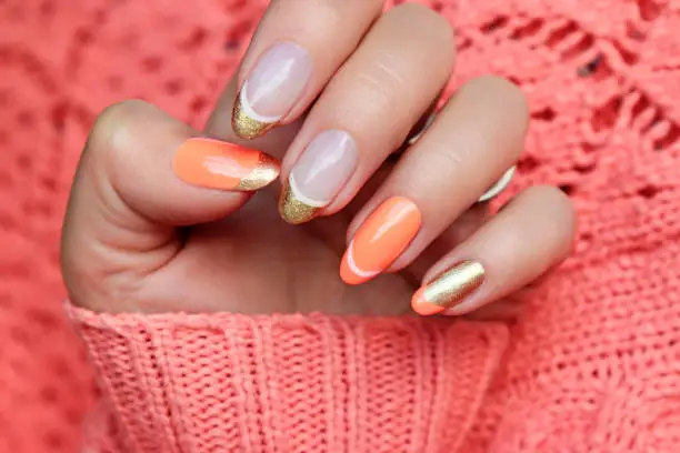 Colorful nail design with peach and golden nail polish. French manicure on a knitted orange background.