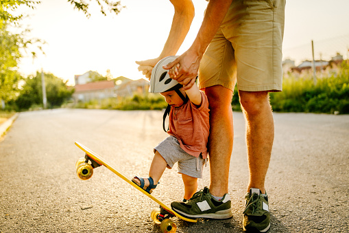 Photo of a baby boy who enjoys his first skateboard ride with a little help from his dad