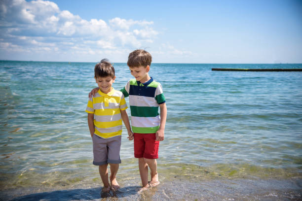 Two adorable little kid boys standing on lonely ocean beach. Child playing and looking on horizon. Vacations, summer, travel concept. Preschool children sibling brother best friends enjoying summer vacations on sea. dos adorables niños de pie en la solitaria playa oceánica. niño jugando y mirando en el horizonte. vacaciones, verano, concepto de viaje. niños en edad preescolar hermano hermano mejores amigos disfrutando de vacaciones de verano en el mar