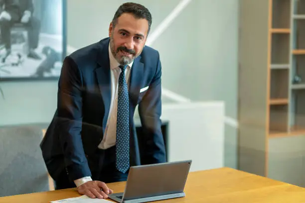 The boss, who checks and takes notes at the computer in his own workroom in the office, the handsome hardworking boss with the beard in the suit, the bank manager, the team leader