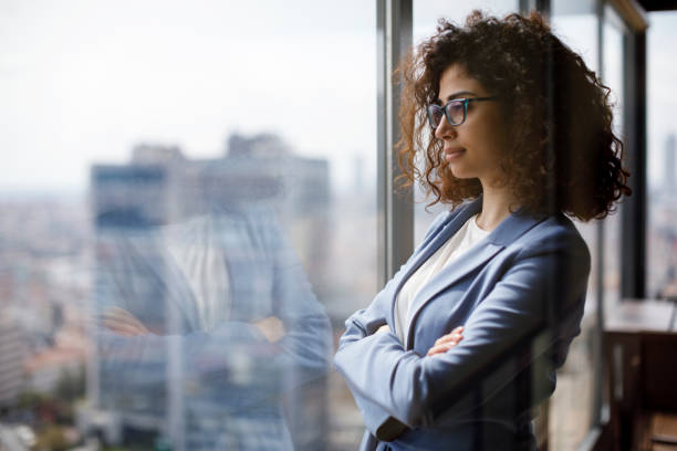 jeune femme d'affaires regardant par la fenêtre - bâtiment vu de photos et images de collection