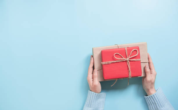 istock Woman Hands holding craft paper gift box on blue background and copy space. for present Christmas, new year, valentine day or anniversary. 1186959219
