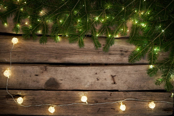 istock Green Christmas tree branches with lights on rough weathered wooden planks 1186965592