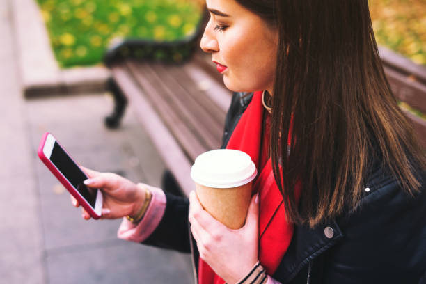 femme s'asseyant sur un banc avec la boisson et le téléphone. - red text messaging cafe teenage girls photos et images de collection