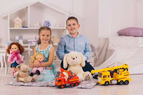 happy caucasian children sitting in their room, boy with car, girl  with doll beautiful happy caucasian children sitting in their room, boy with car, girl  with doll girl playing with doll stock pictures, royalty-free photos & images