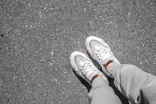 white sneakers walking on concrete. Sneakers on the pavement. Top view of legs on asphalt