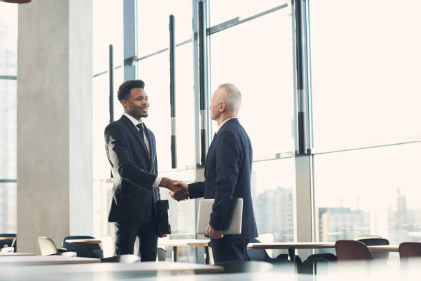 istock Cheerful handsome young African-American businessman in suit making handshake while greeting crisis manager into company 1186986814