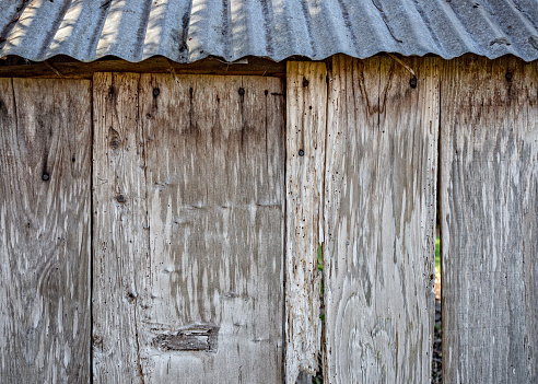 Side of old wood shed with tin roof. Rustic and weathered wood planks with rusty nails.