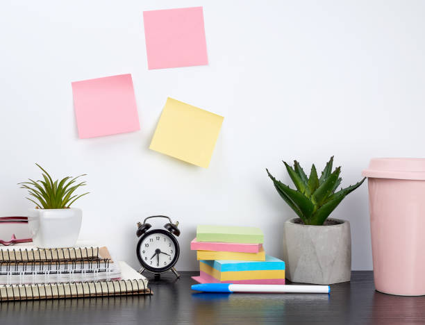 istock stack of spiral notebooks and colored stickers, next to a ceramic pot with a flower on a black table 1186989033