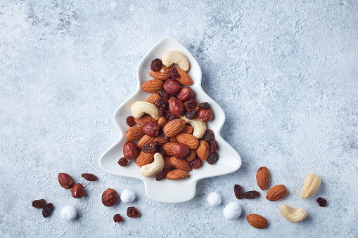 dried fruit and nuts on fir shape plate, christmas snack on painted gray background, top view