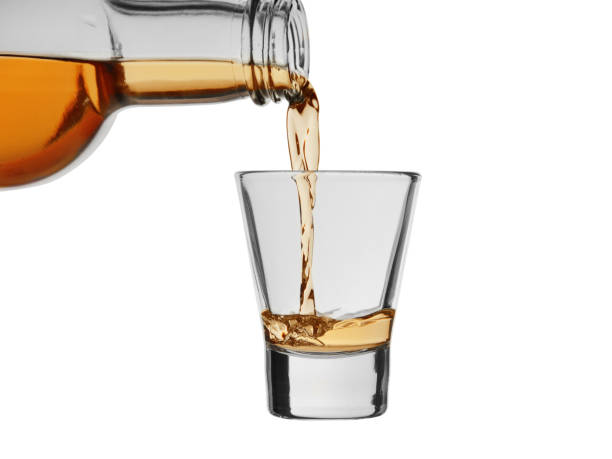 istock Strong alcoholic drink pour from a bottle into a wineglass isolated on a white background 1186995194