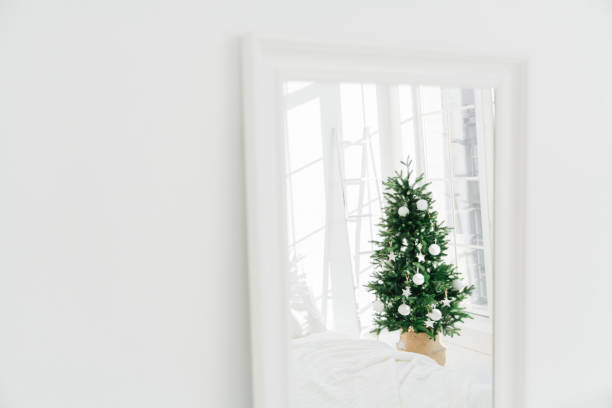 istock Decorated Christmas tree reflecting in mirror, white spacious room. Bedroom with New Year decoration. Modern classic style. Christmas eve at home 1186996315