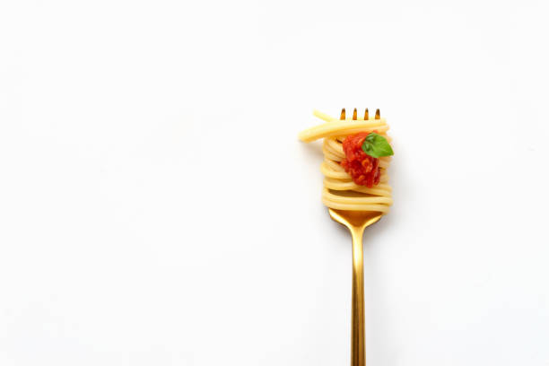 Top view of gold fork with spaghetti, tomato, and basil on white