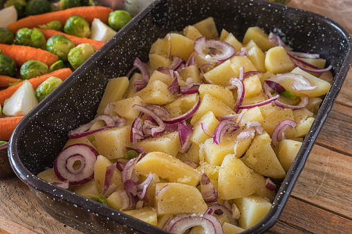 Half boiled potato with fresh red onions in casserole dish, ready for roasting, close-up, no people