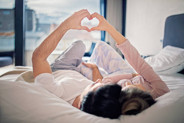 Couple is lying on the bed and making heart with their hands stock photo